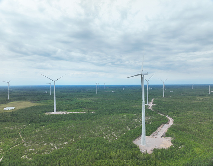 Ilmakuva tuulivoimaloista, taustalla näkyy metsää ja taivasta.