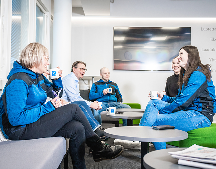 Smiling people sit on a sofa chatting and drinking coffee.