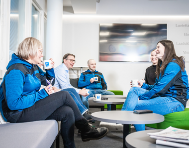 Smiling people sit on a sofa chatting and drinking coffee.