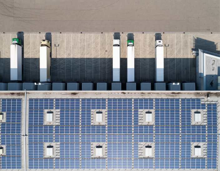 Aerial view – solar panels on logistics hall roof, trucks parked in front.
