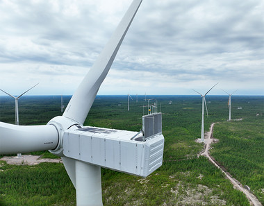 Kuvan etualalla tuulivoimalan lavat, taustalla näkyy lisää tuulivoimaloita, autoteitä ja metsää.