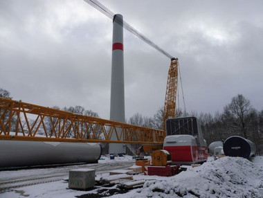 Kran und Großkomponenten einer Windenergieanlage lagern auf der Baustelle neben dem teils fertiggestellten Turm