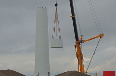 Ein Kran hebt einen Betonring neben dem entstehenden Turm in die Höhe