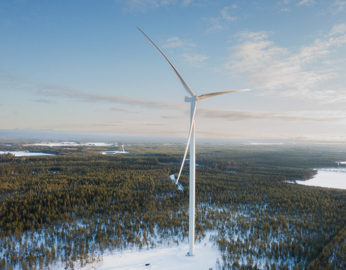 Tuulivoimala, jonka taustalla näkyy lumista metsämaisemaa ja sininen taivas.