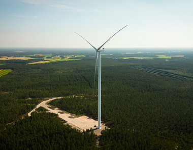 Tuulivoimala metsän keskellä, taustalla pilviä.