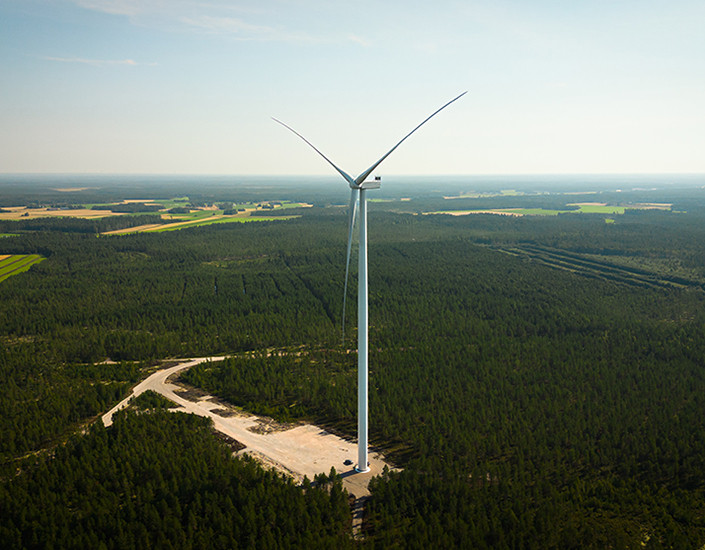Tuulivoimala metsän keskellä, taustalla pilviä.