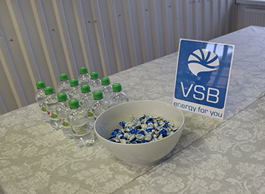 Pöydän päällä vesipulloja, kulhollinen makeisia ja VSB:n logo.